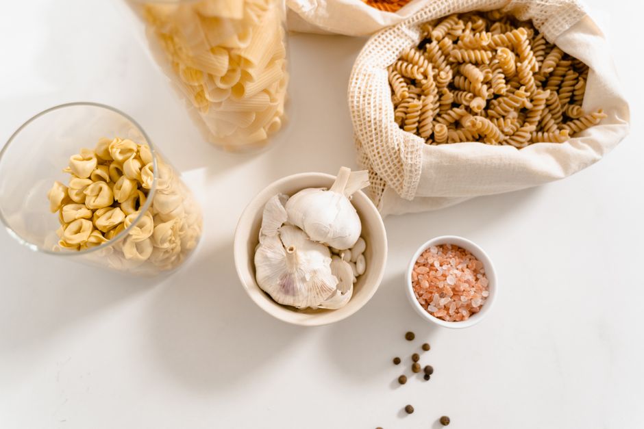A top view of organic pasta ingredients and seasonings, featuring garlic, pink salt, and reusable bags.