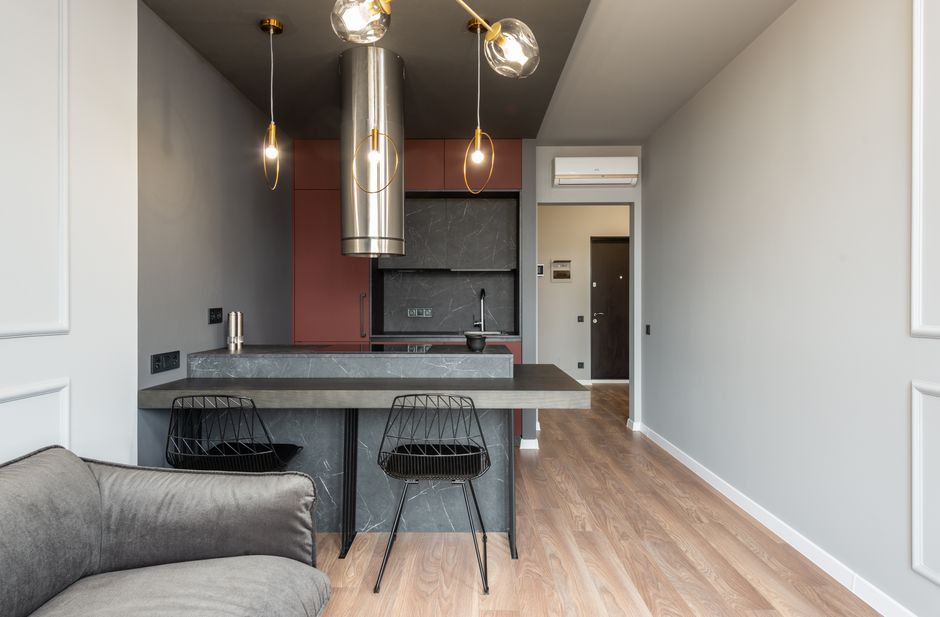 Contemporary interior design of modern apartment with open space kitchen with island countertop under pendant lamps and tube range hood