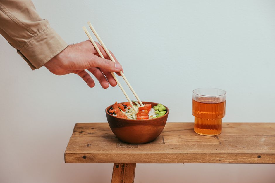Hand reaching for a colorful rice bowl with edamame and cherry tomatoes with tea.